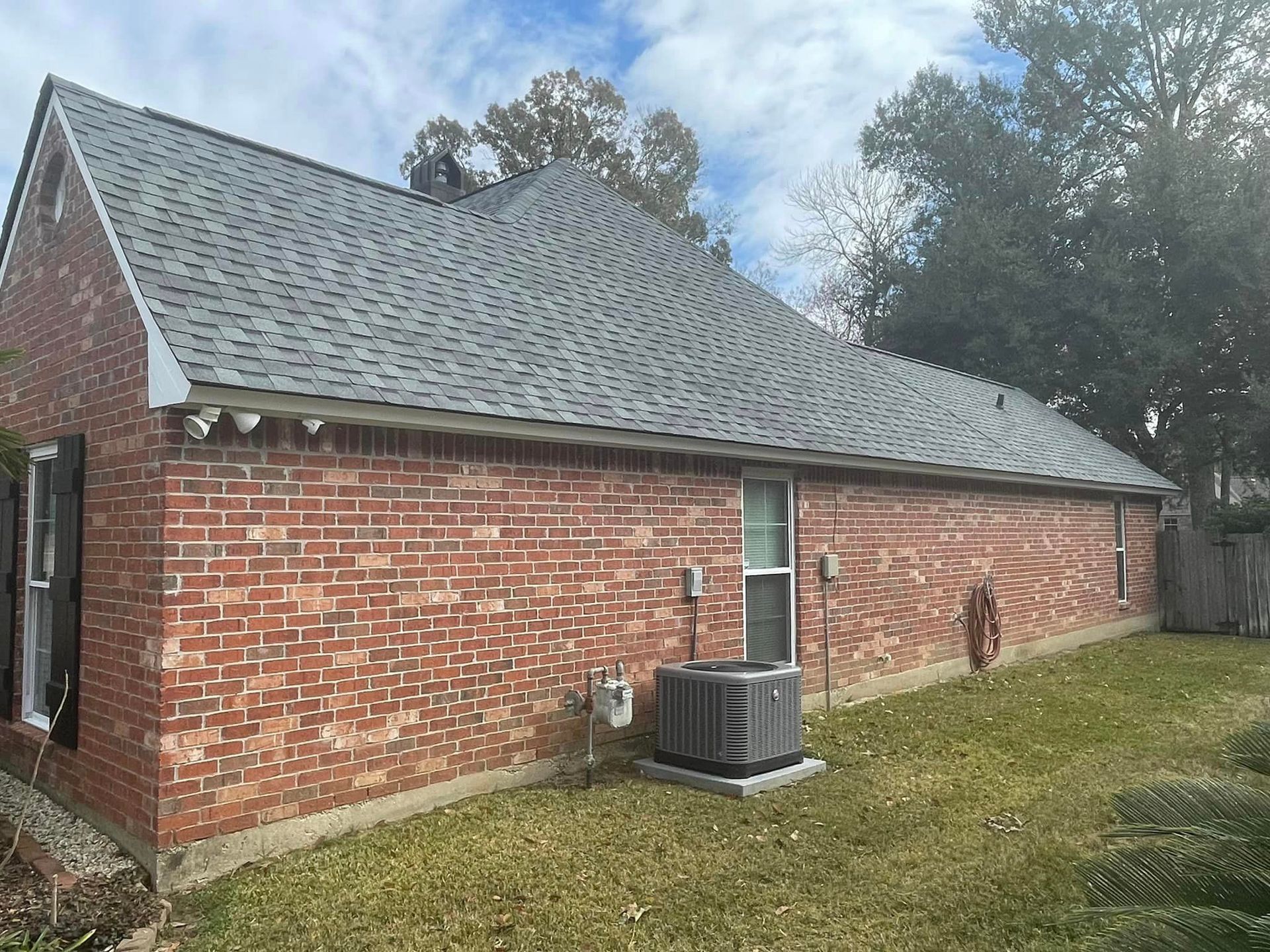 A brick house with a gray roof and a air conditioner in the backyard