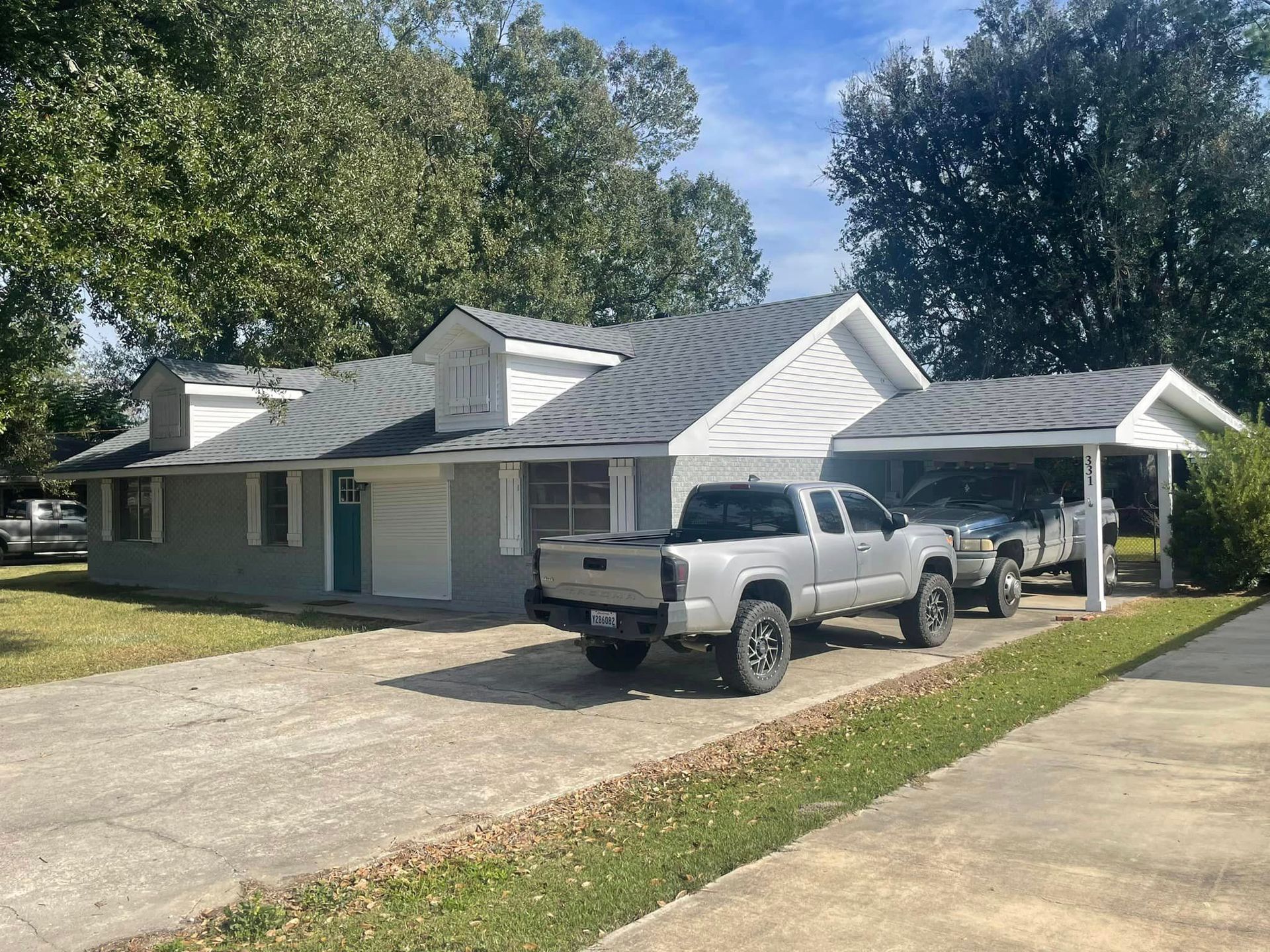Two trucks are parked in front of a house with a carport
