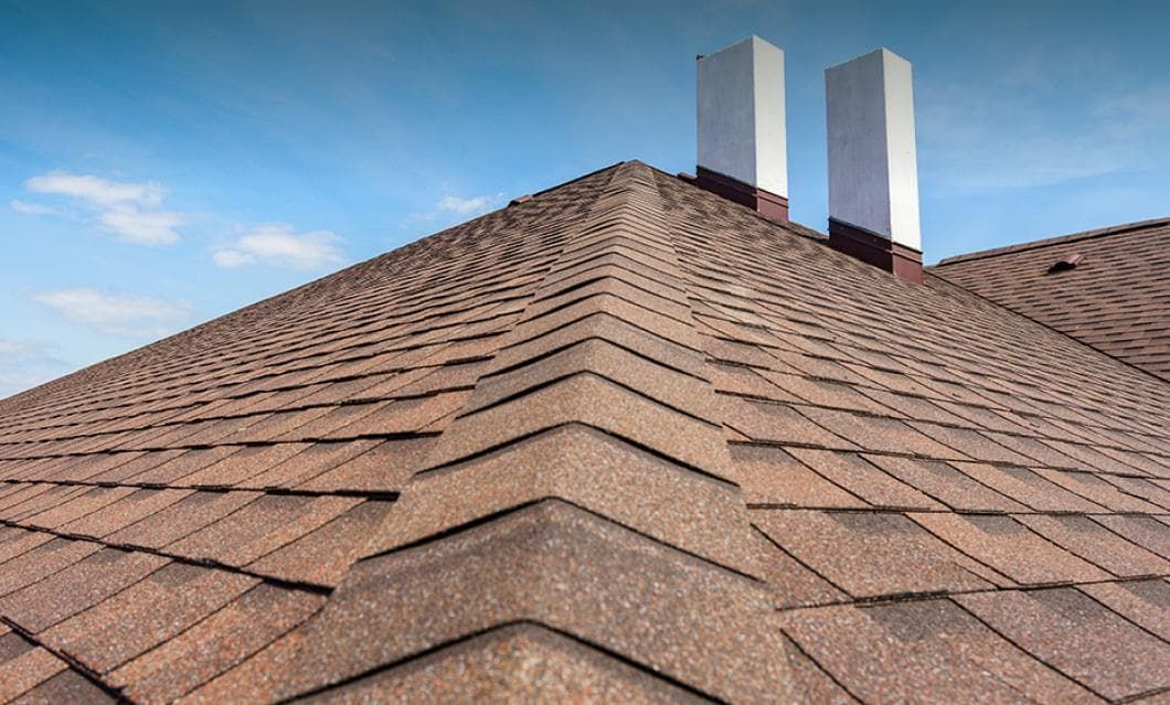 A roof with two chimneys on it and a blue sky in the background