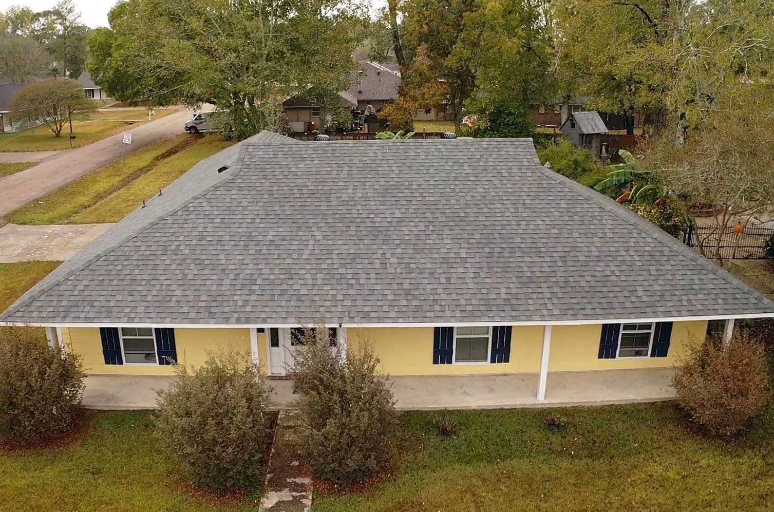 An aerial view of a yellow house with a gray roof and blue shutters
