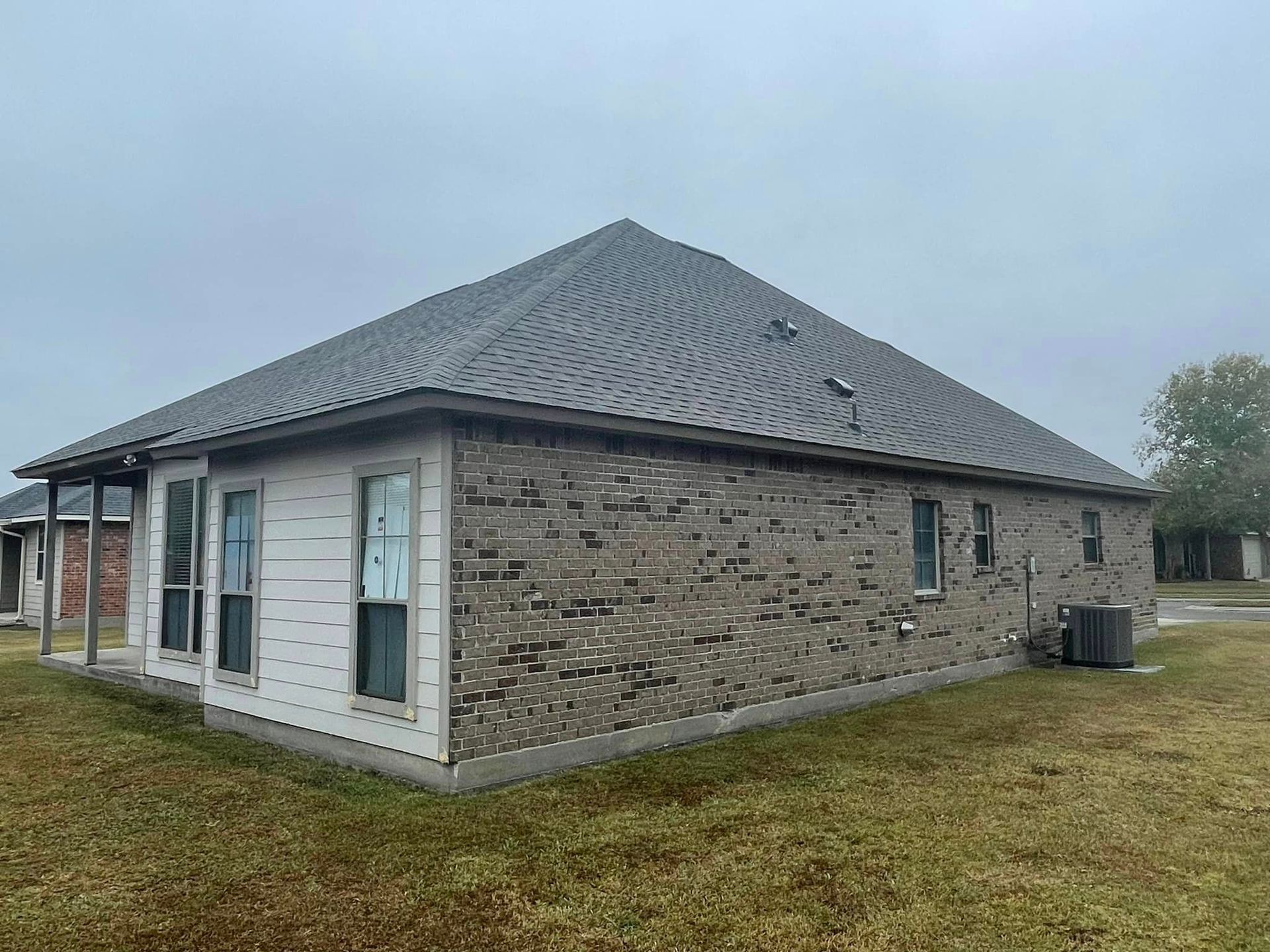 A small brick house with a gray roof is sitting on top of a lush green field