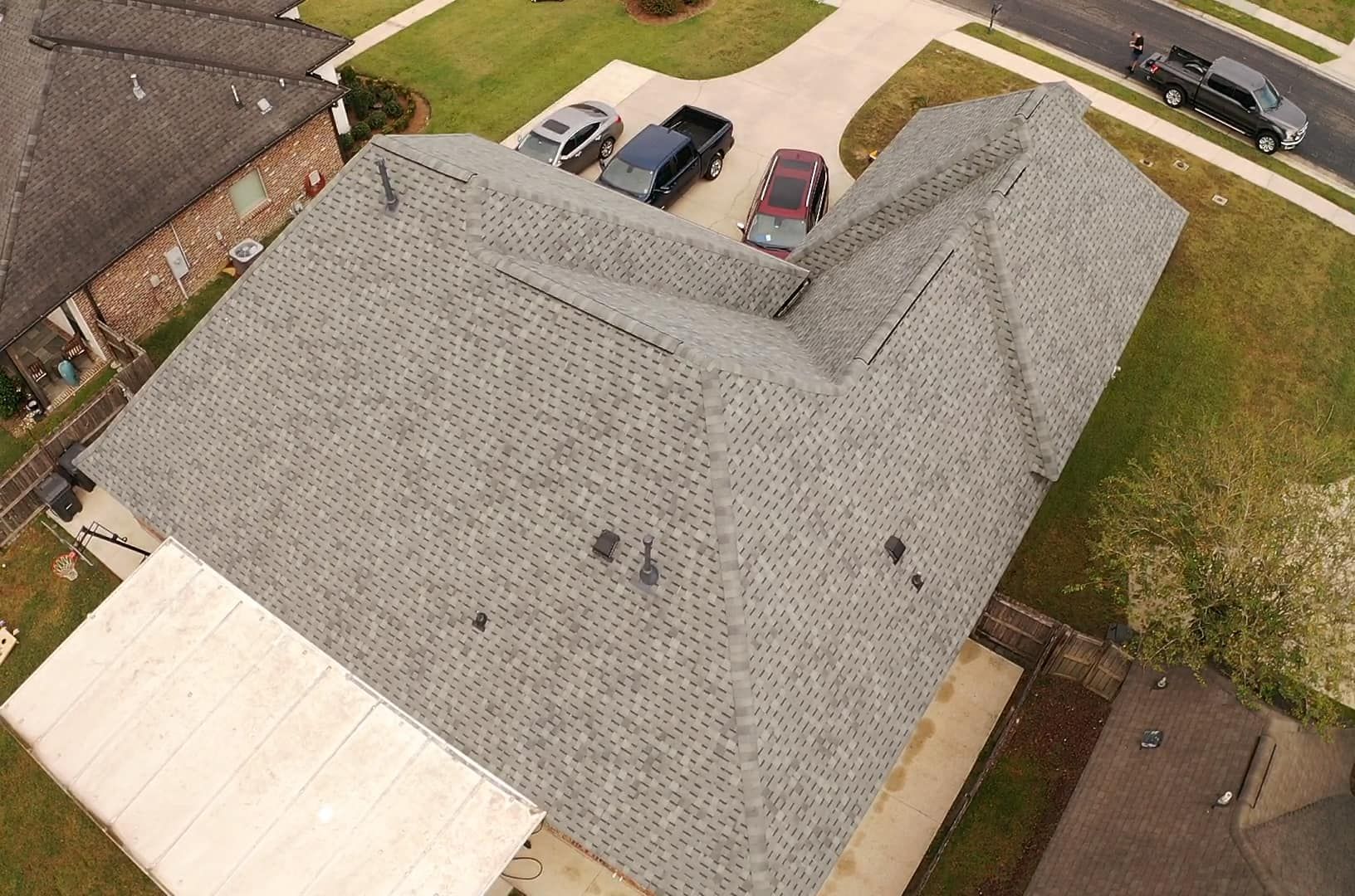 An aerial view of a house with a gray roof and cars parked in front of it