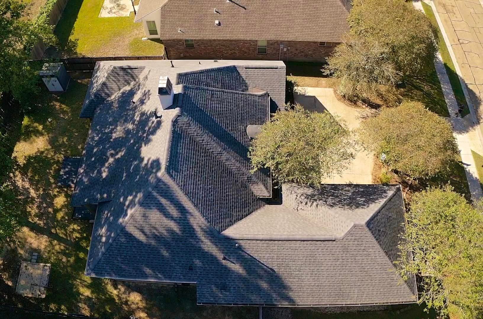 An aerial view of a house with a black roof surrounded by trees