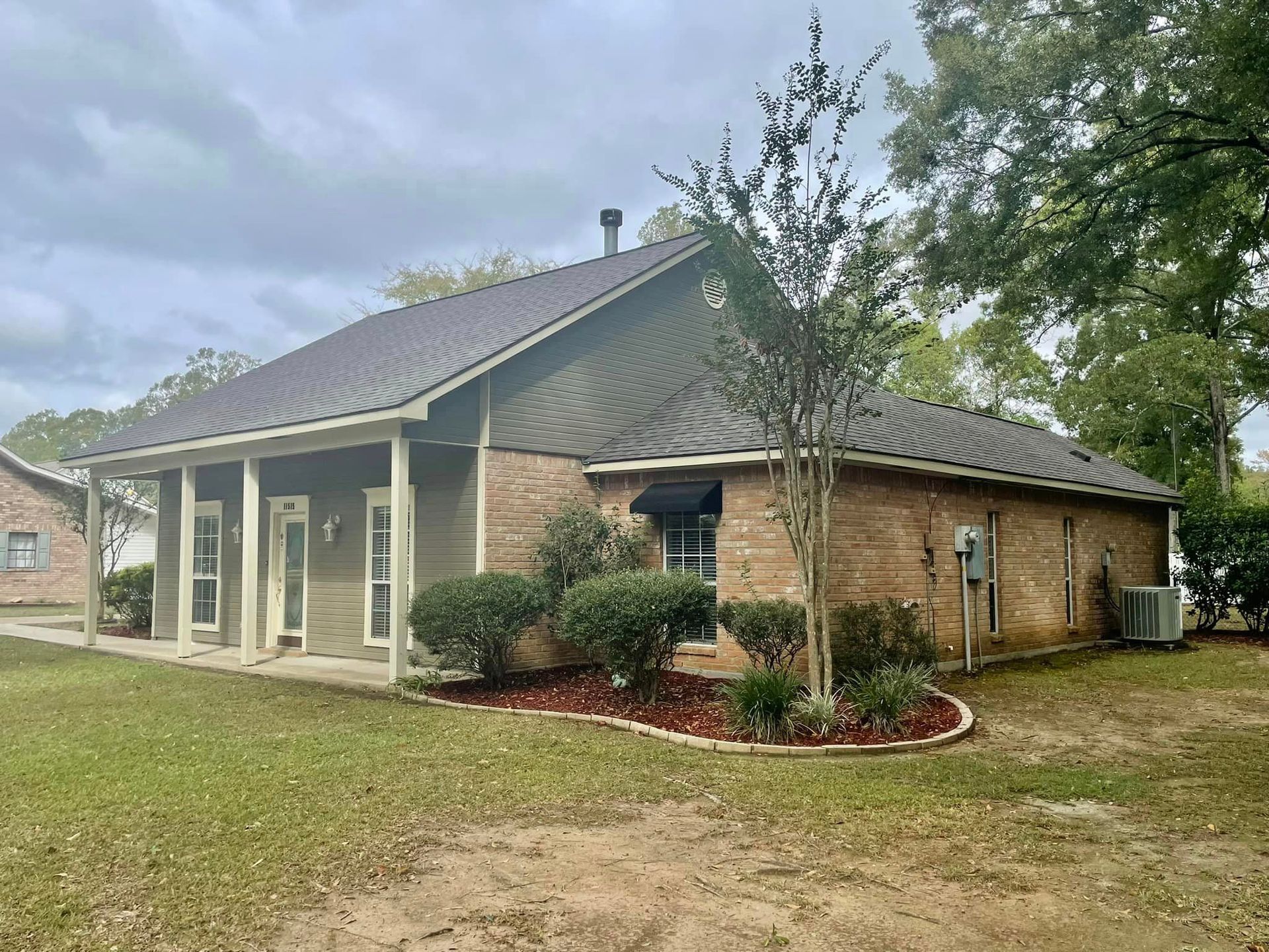 A brick house with a gray roof and a large lawn in front of it