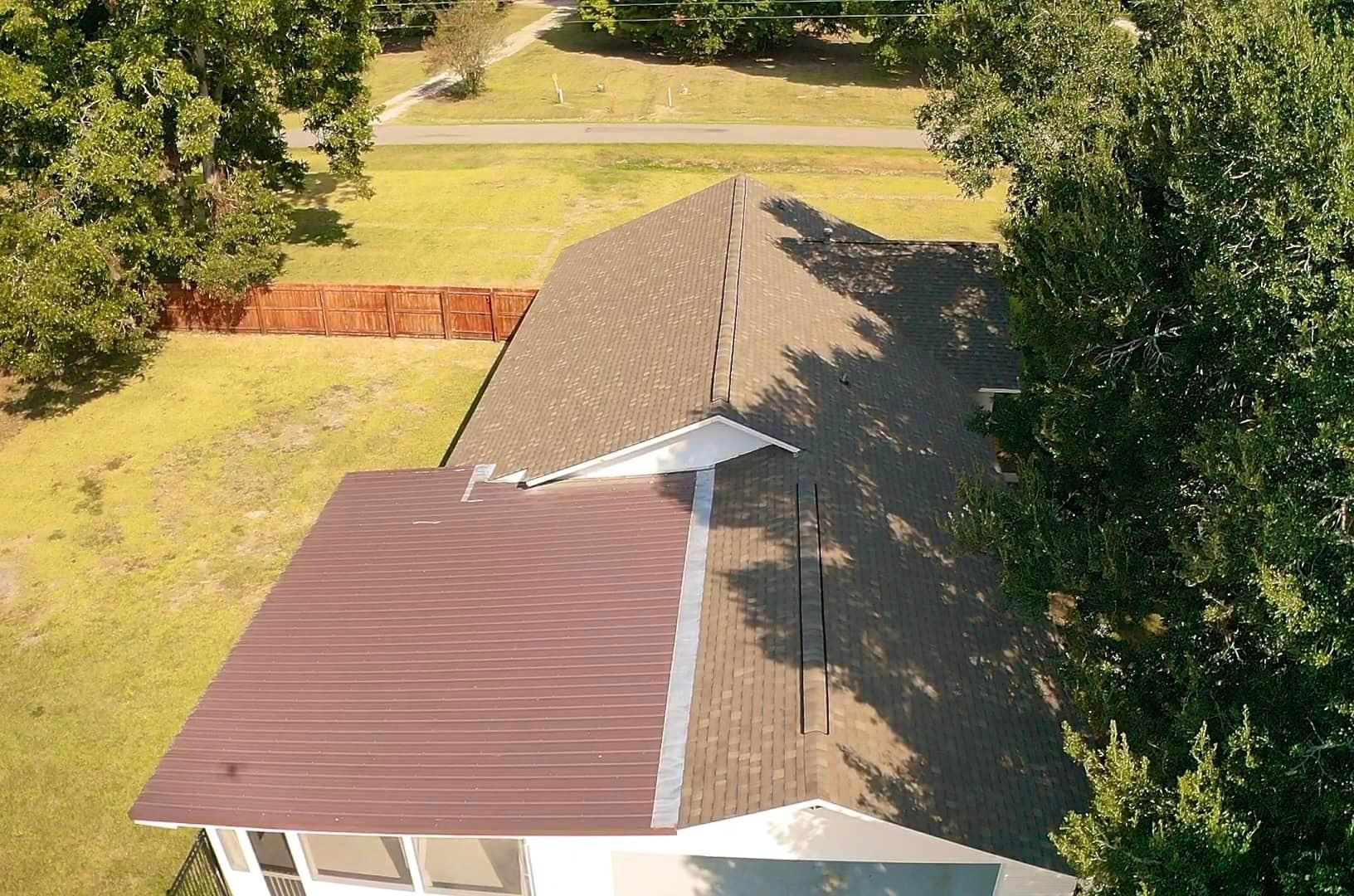 An aerial view of a house with a brown roof surrounded by trees