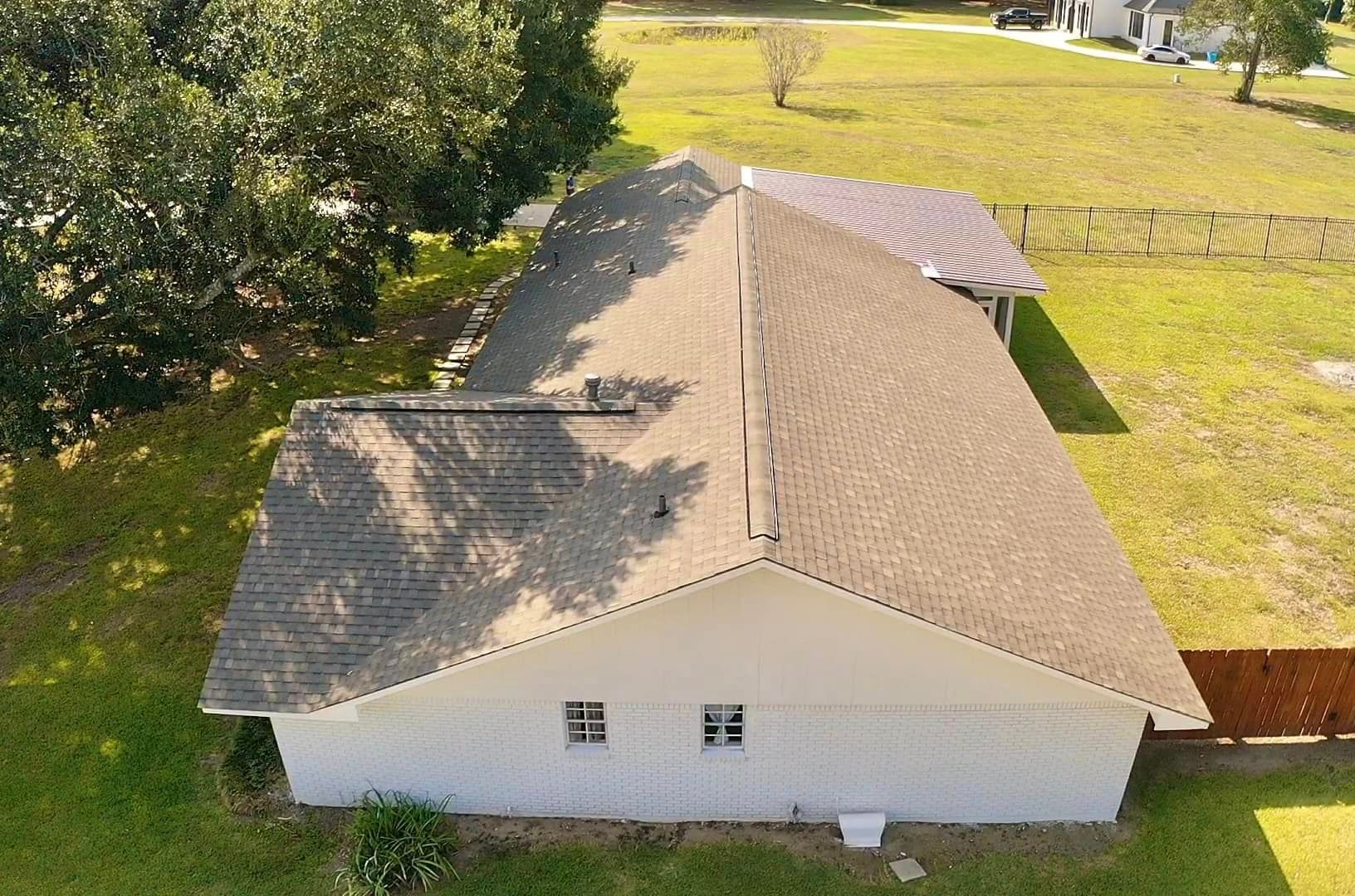 An aerial view of a white house with a brown roof surrounded by grass and trees