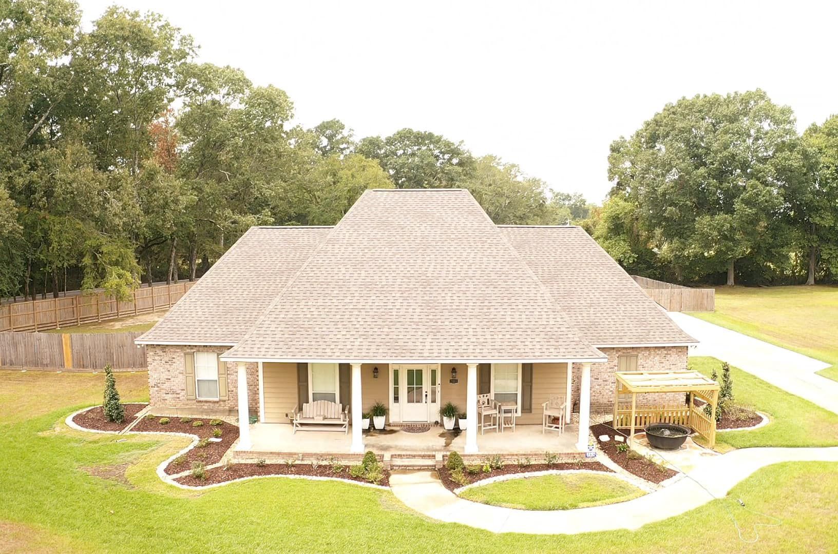An aerial view of a house with a porch and trees in the background
