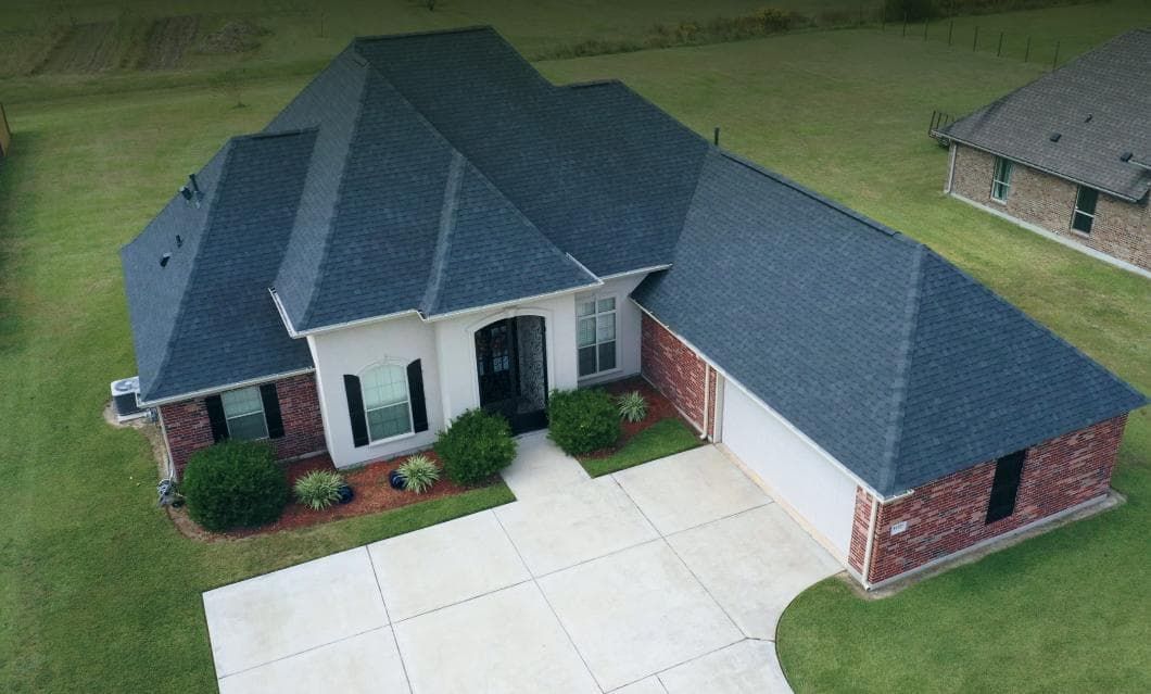 An aerial view of a brick house with a blue roof and a driveway