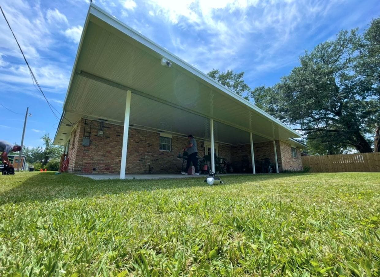 A man is standing under a covered porch in front of a brick house