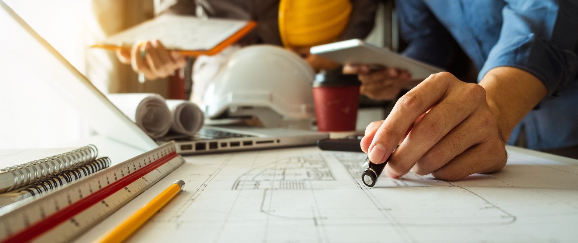 A person is sitting at a table drawing a blueprint.