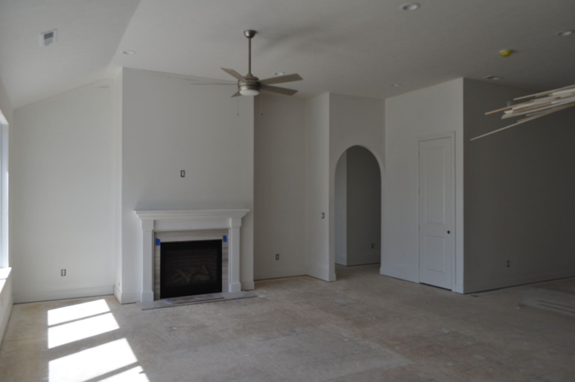 Empty living room with a white fireplace, ceiling fan, arched doorway, and closet doors.
