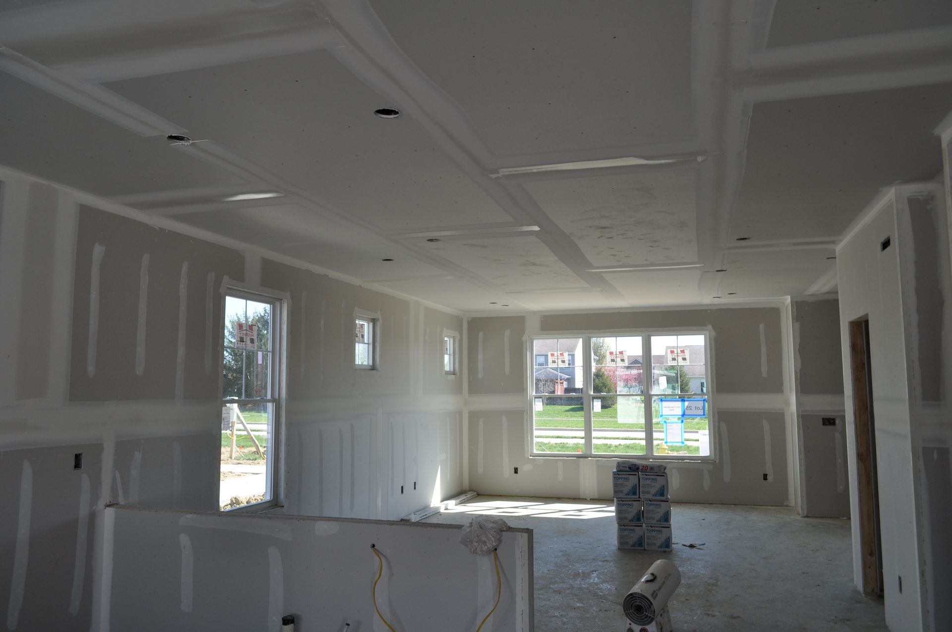 Unfinished drywall interior of a bright room with large windows and a door opening to a yard.