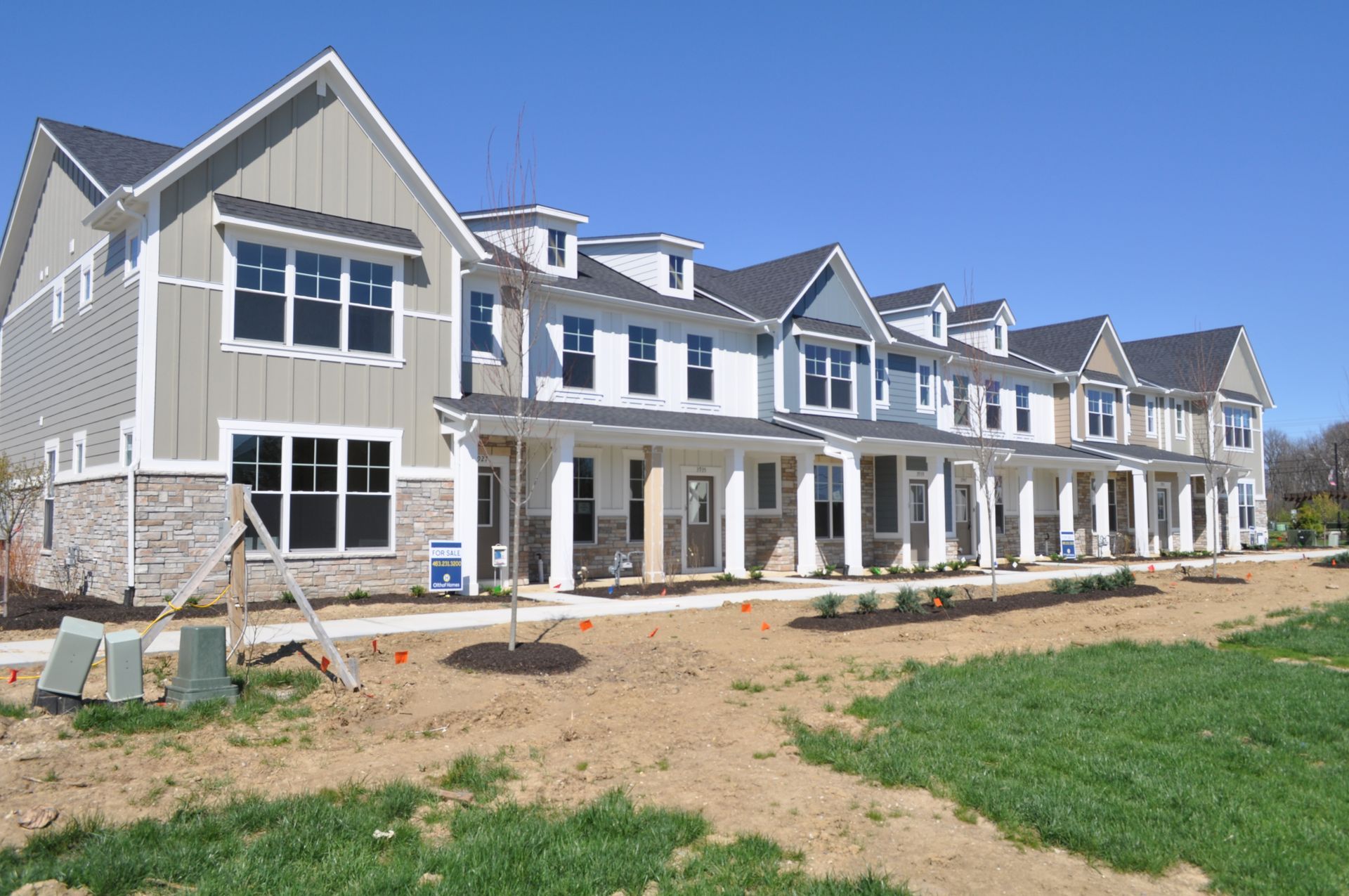 Row of new gray-and-white townhouse-style homes under construction on a sunny day
