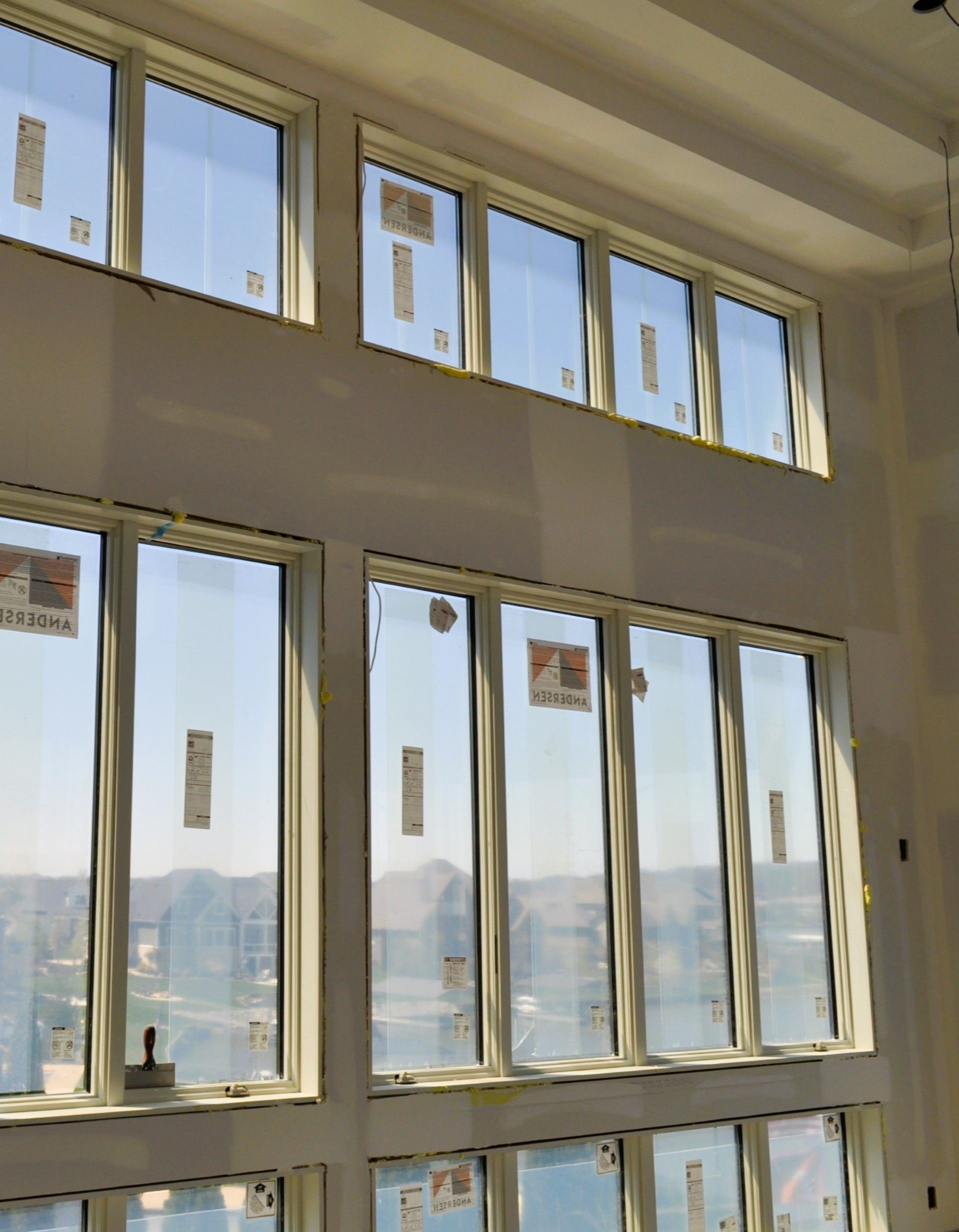 Large, multi-pane windows with paper stickers installed in a room with unfinished drywall and high ceilings.