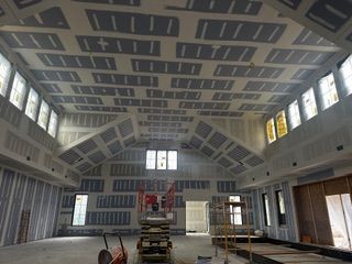 Interior of a building under construction, showing drywall installation on walls and ceiling; windows, lift.