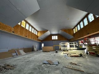 Interior construction of a large room. Gray walls and ceiling, stained-glass windows, and construction materials are visible.