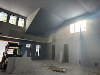 Interior of a room under construction with high, angled ceiling, unfinished walls, and natural light.