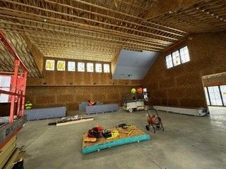 Interior of a building under construction, showing exposed wood framing, windows, and construction materials.