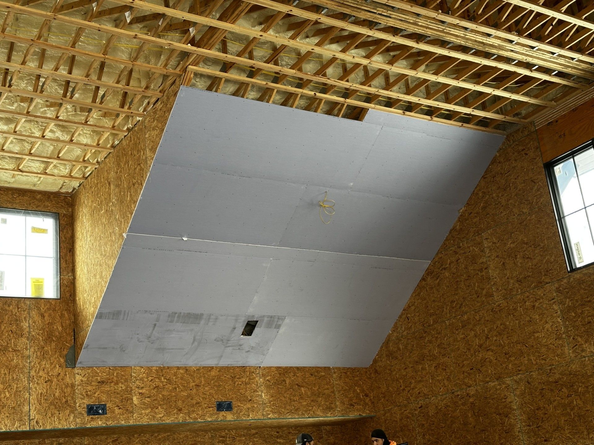 Interior view of a room under construction with exposed wood framing and drywall partially installed on angled ceiling.