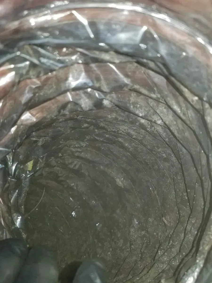 Inside view of a flexible air duct, coated in visible dark grime.