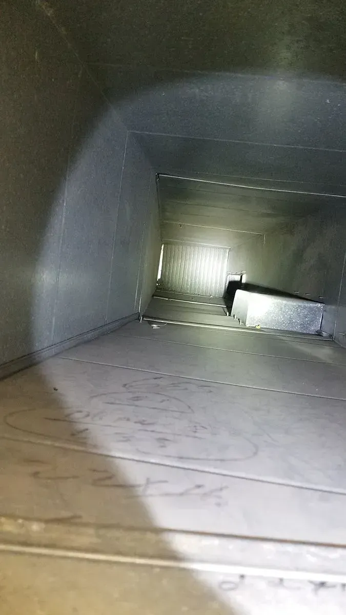 Inside of a rectangular duct, light shining, showing seams and some debris.