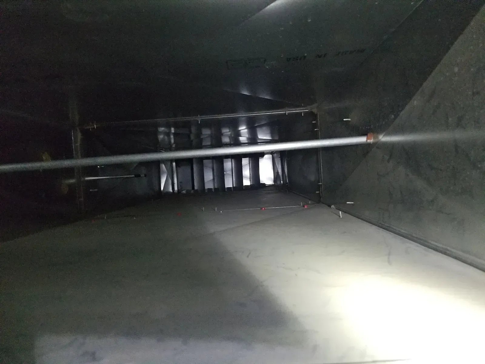 Inside of a dark duct. The light is focused on the end. A pipe runs across the center.
