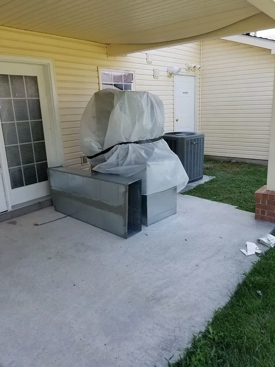 Metal HVAC components and units under cover on a patio beside a building.