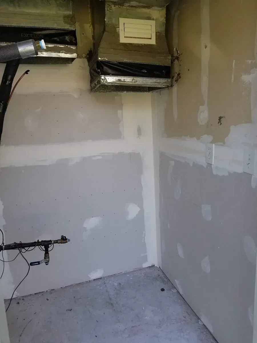 Unfinished room with drywall, a vent, and exposed pipes near the ceiling and walls.