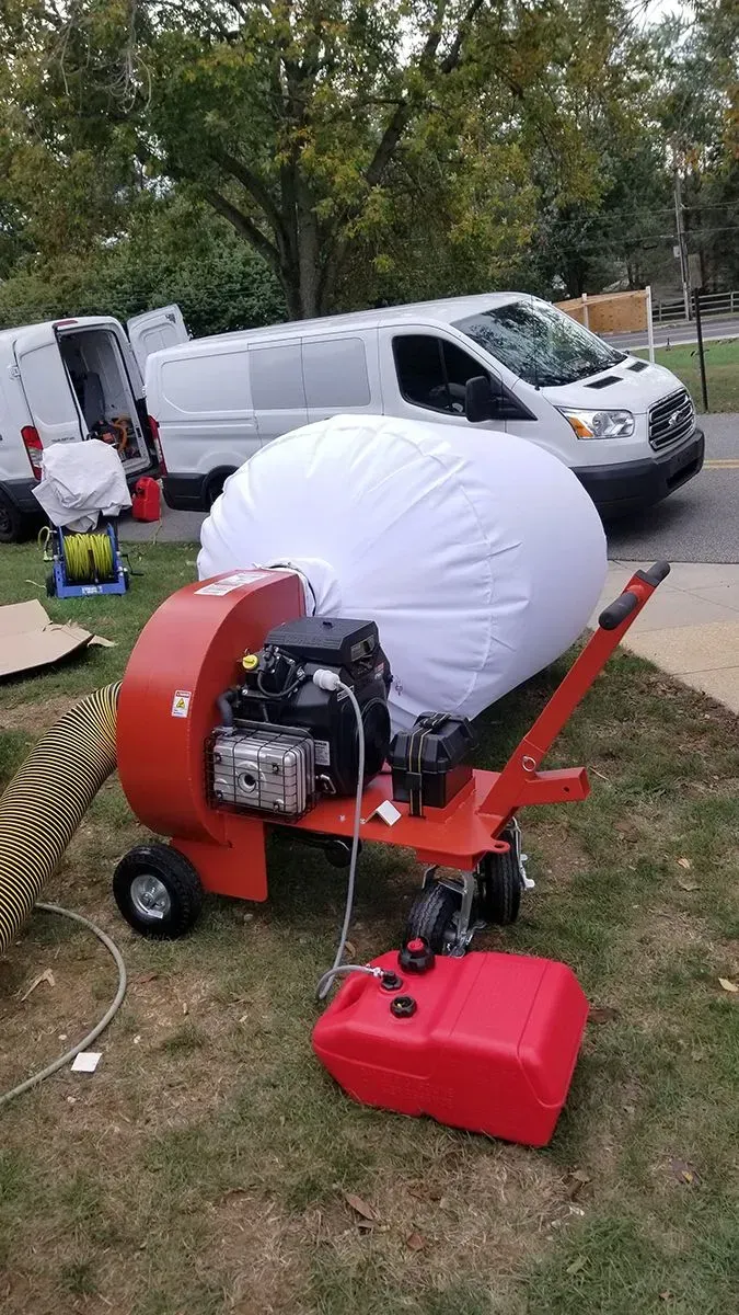Red leaf vacuum and collection bag on grass, white van in background.