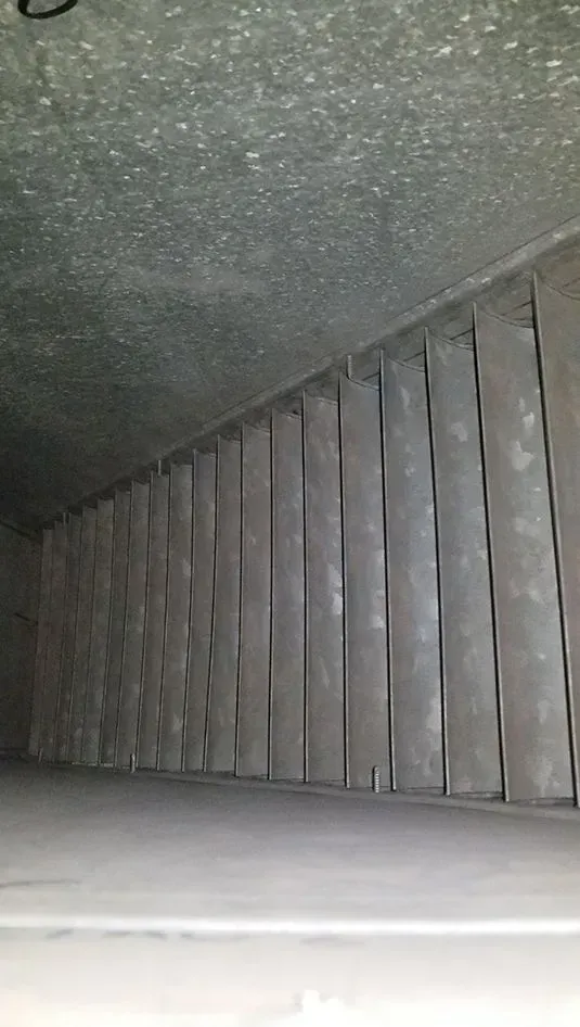 Inside of a rectangular duct with numerous vertical metal baffles. The interior appears dusty.