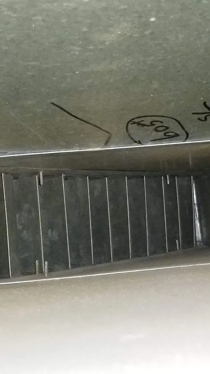 Metal grid below a surface with handwritten markings, including 