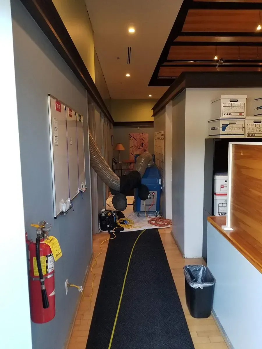 Narrow hallway with blue-gray walls, fire extinguisher, and workers. Black carpet and yellow cord.