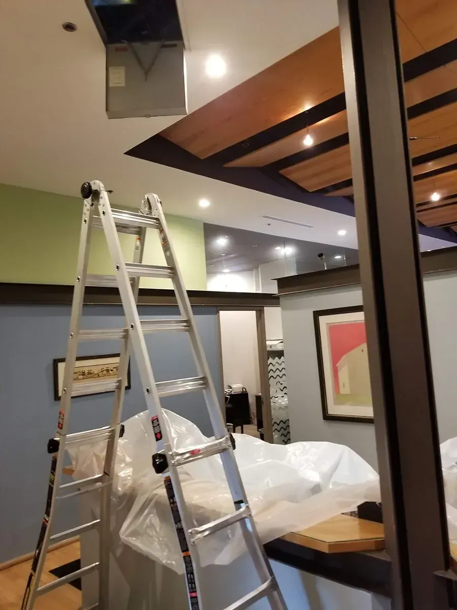 A stepladder beneath a ceiling vent during an interior renovation. Blue, green, and wood tones.