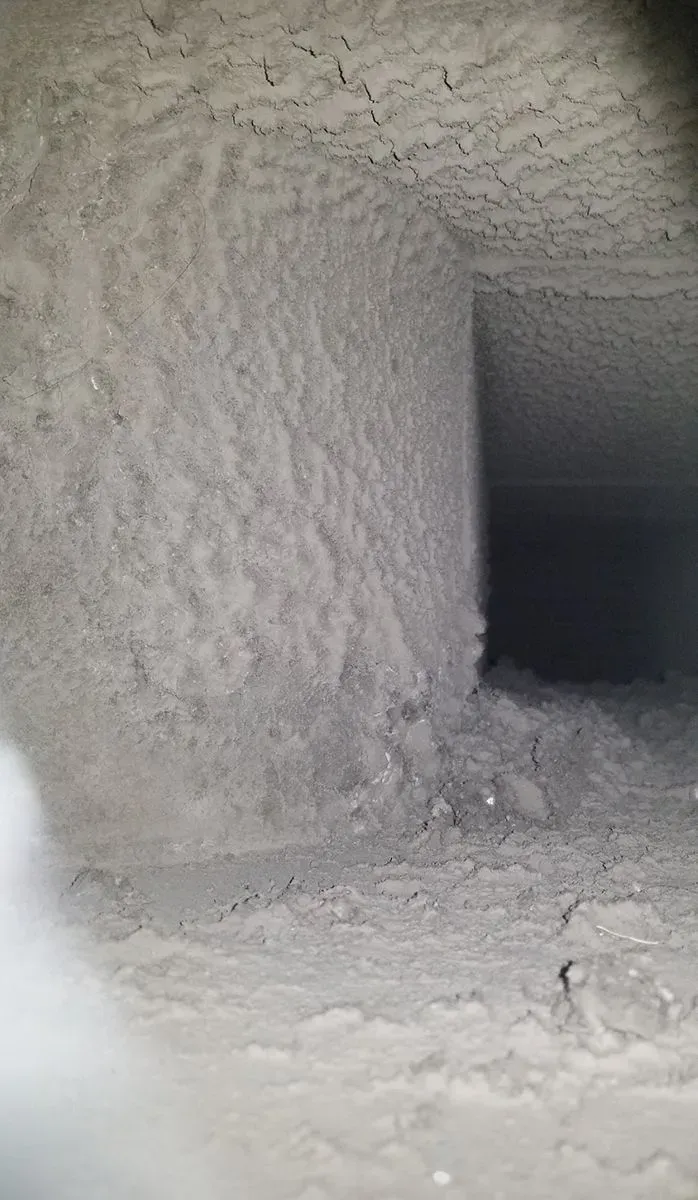 Inside of an air duct, covered with thick white dust. A rectangular opening is visible.
