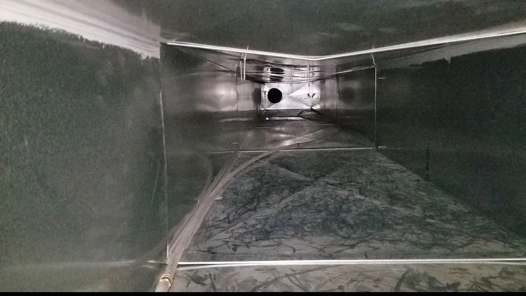 Inside view of a metallic air duct. The duct is rectangular, reflecting light. There is a dark, circular opening in the distance.