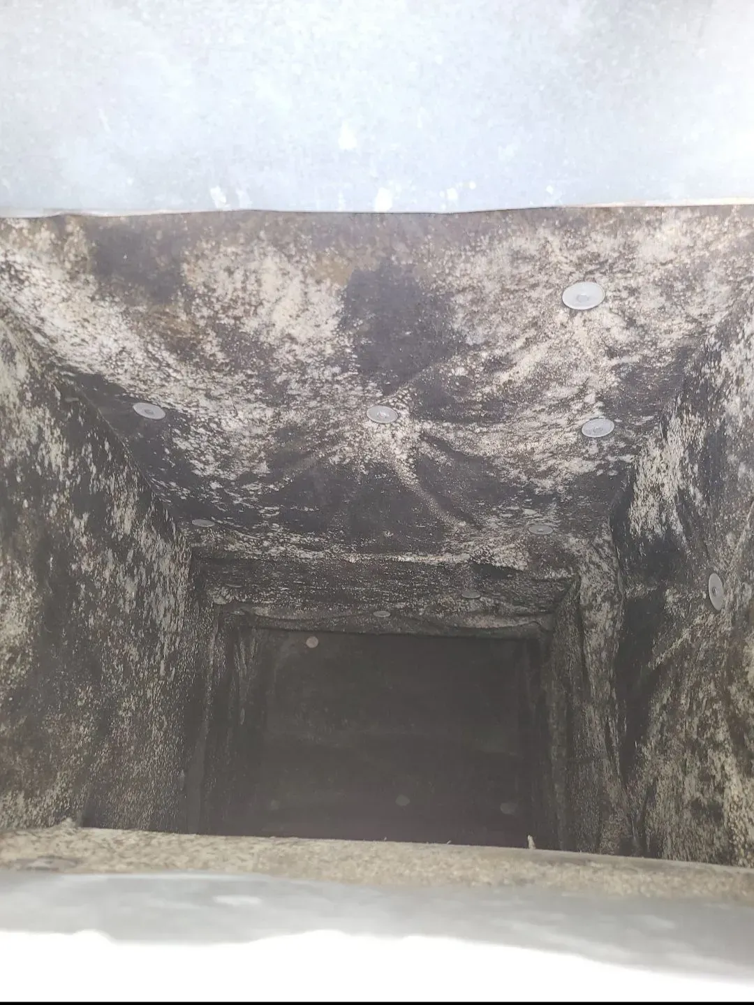 Looking down into a dark, square shaft, with moldy, textured walls and a gray opening at the bottom.