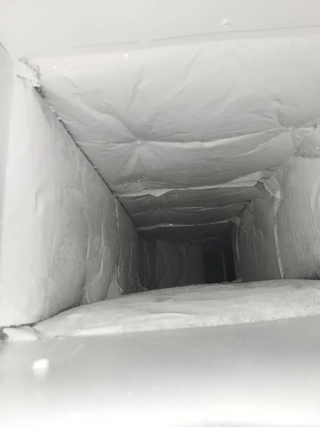 Inside a duct, visible ice buildup on walls. The interior appears rectangular and narrow, leading to darkness.