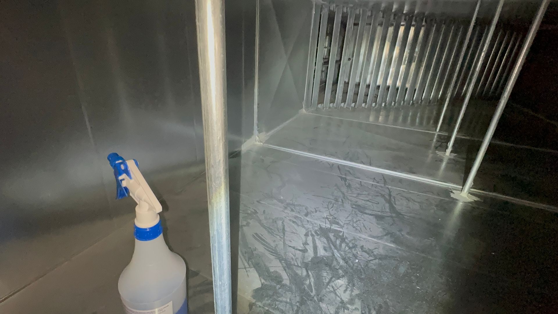 Inside of ductwork, spray bottle resting on floor, spraying. Metal grates and supports.