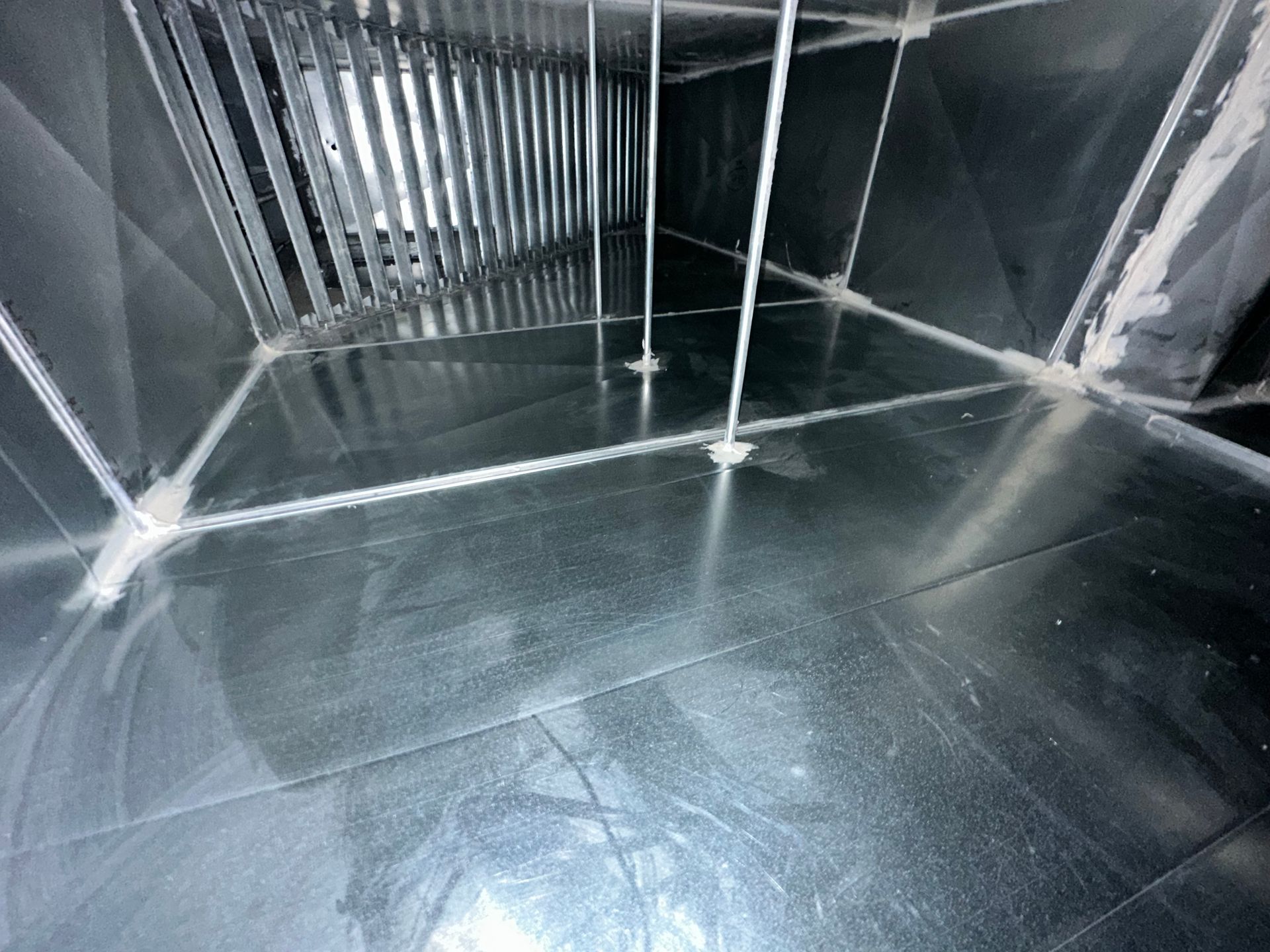 Inside view of an HVAC duct; shiny metal with white supports and some dust.