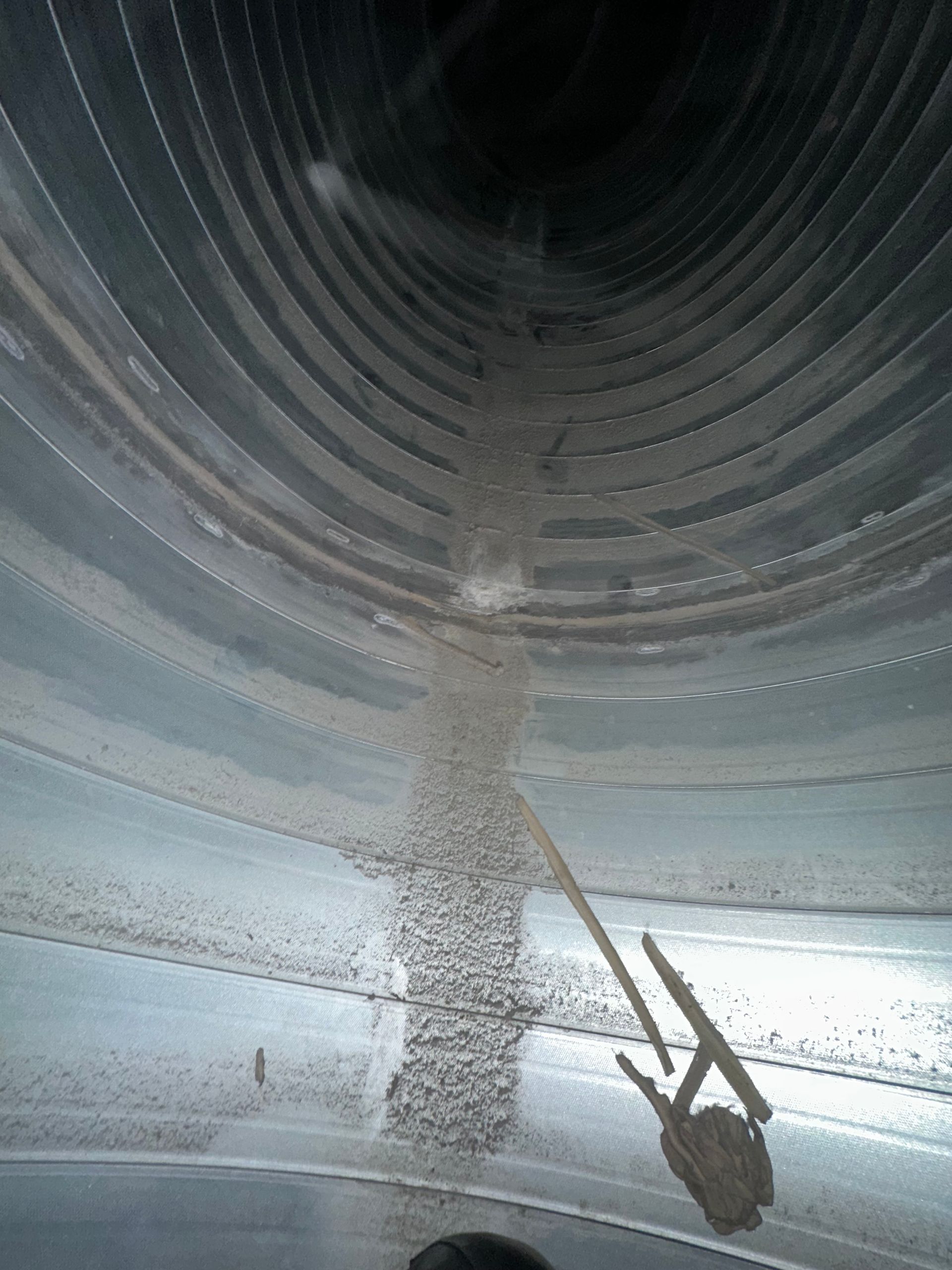 Inside of a cylindrical metal structure, dusty, with a tool hanging down.