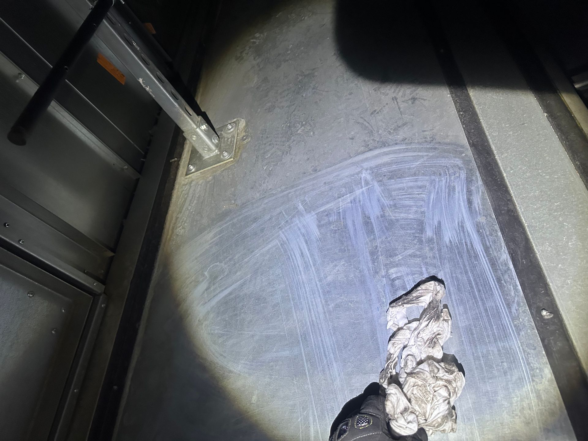 Dark interior with a metal surface showing white streaks, a dirty cloth, and a ladder partially visible.