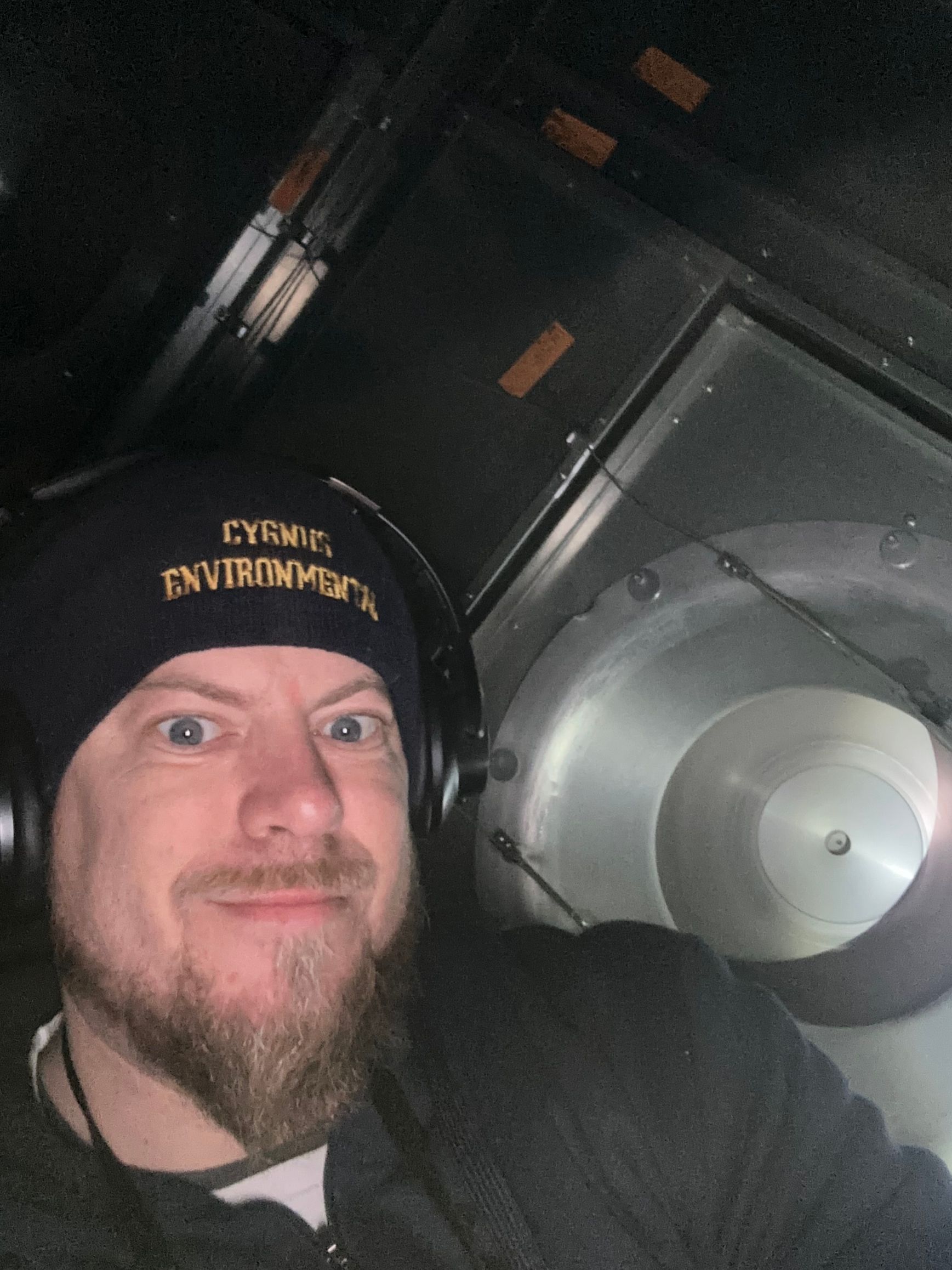 Man wearing a beanie and headphones, making a face inside of a dark, industrial setting.
