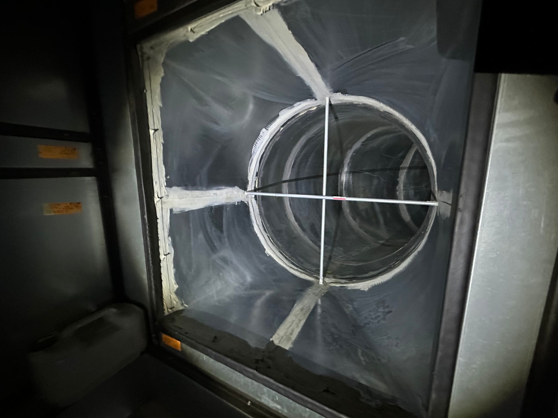 Inside of a metal HVAC duct, a circular opening is fitted with a cross for measuring airflow.