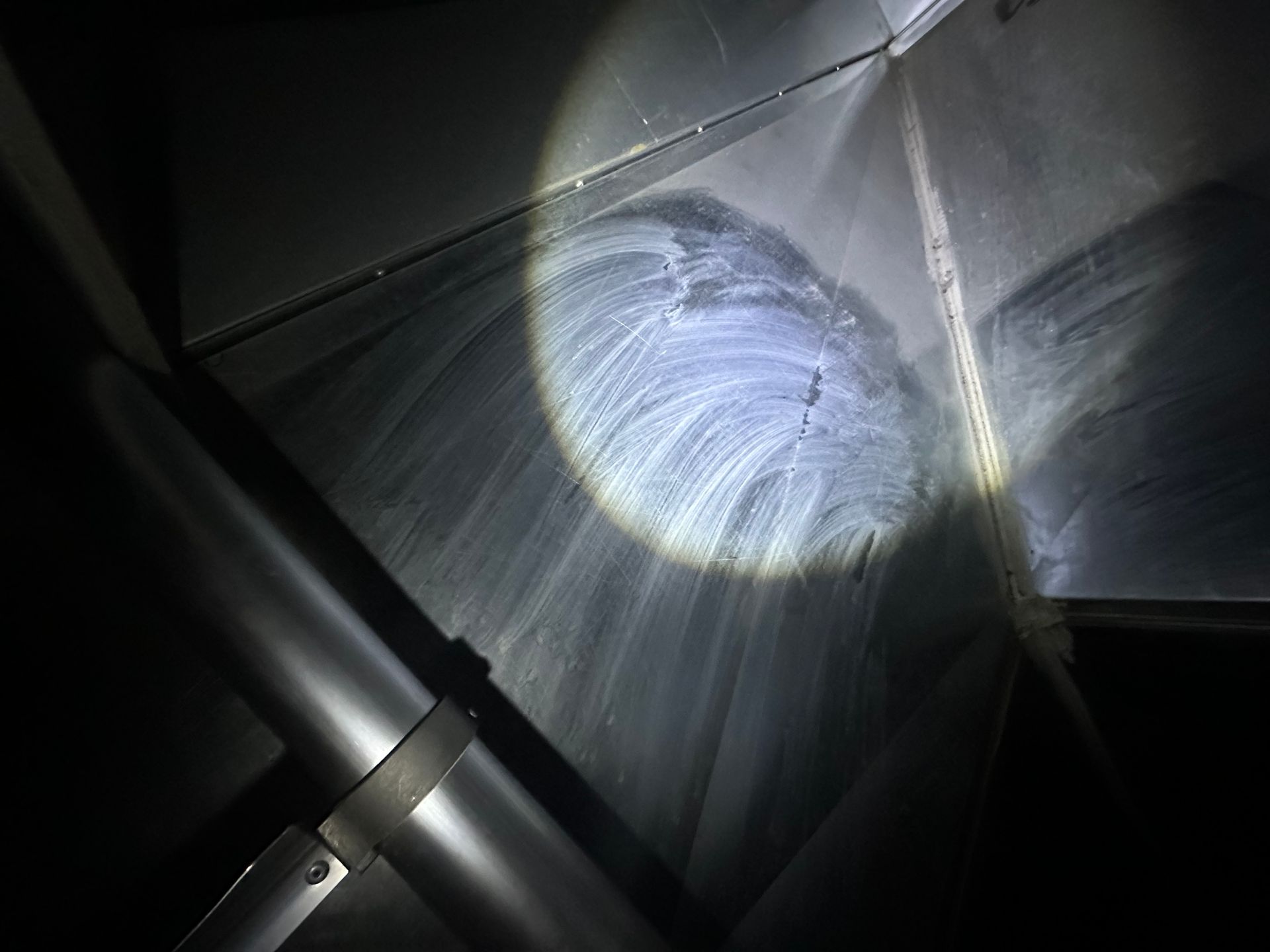 Interior of a metallic air duct with white residue and a crack, illuminated by a spotlight.