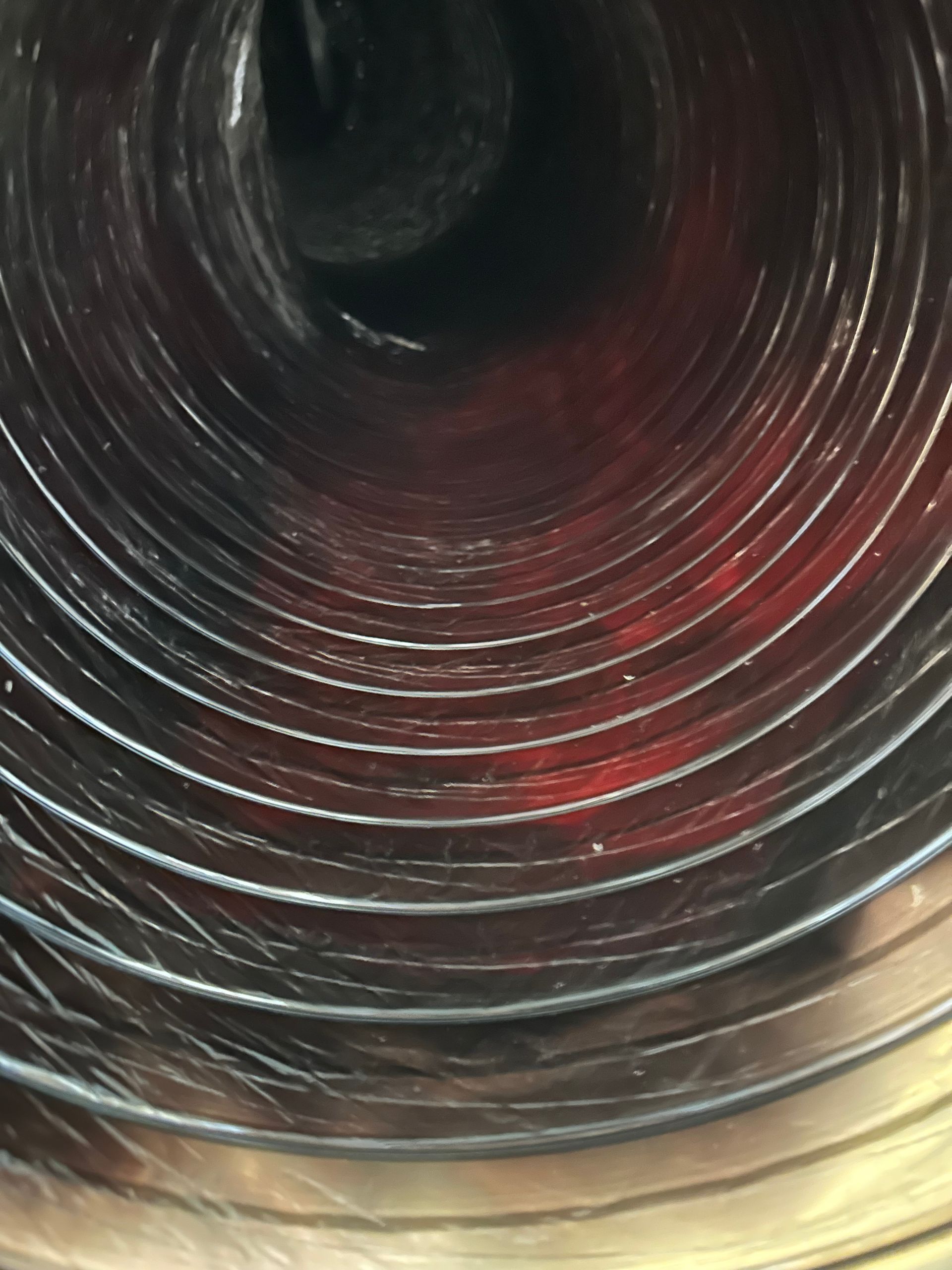 Interior view of a flexible metallic air duct; spiral construction; red and silver hues.