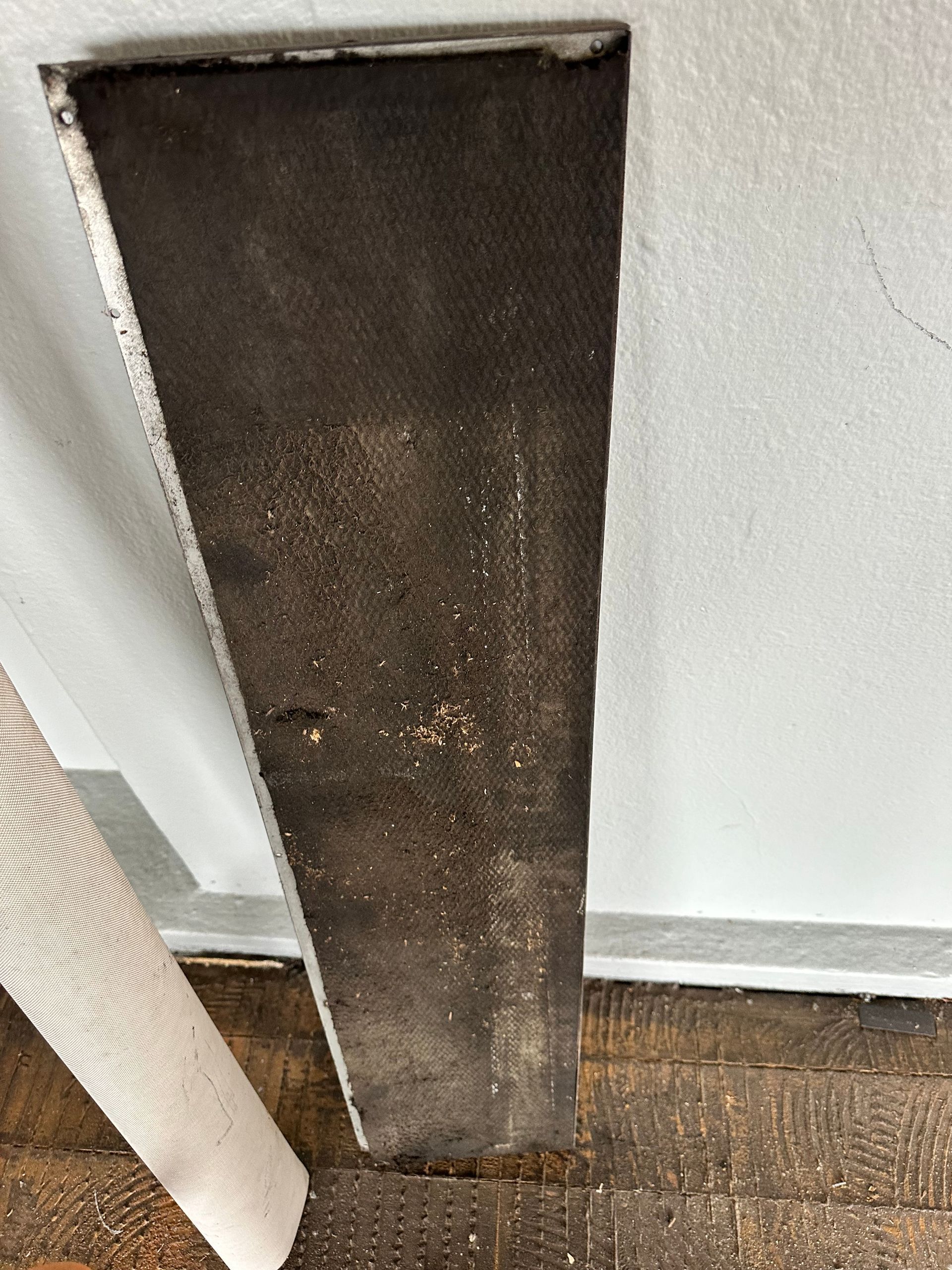 A dark, rectangular, stained piece of material is set in a wall.  A white, patterned roll of material rests below it.