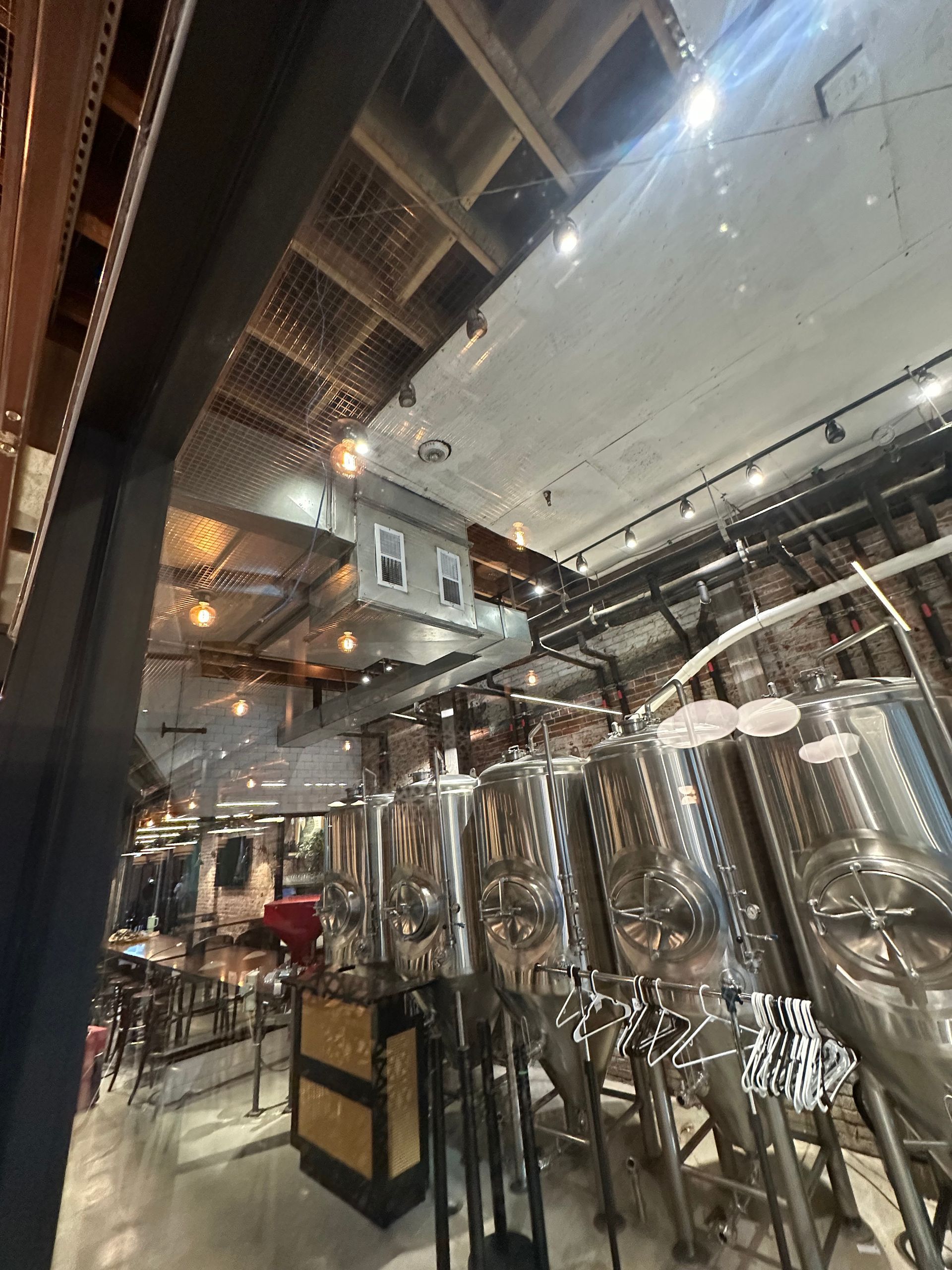 Interior of a brewery. Stainless steel tanks, exposed ceiling, bar area with tables and chairs.