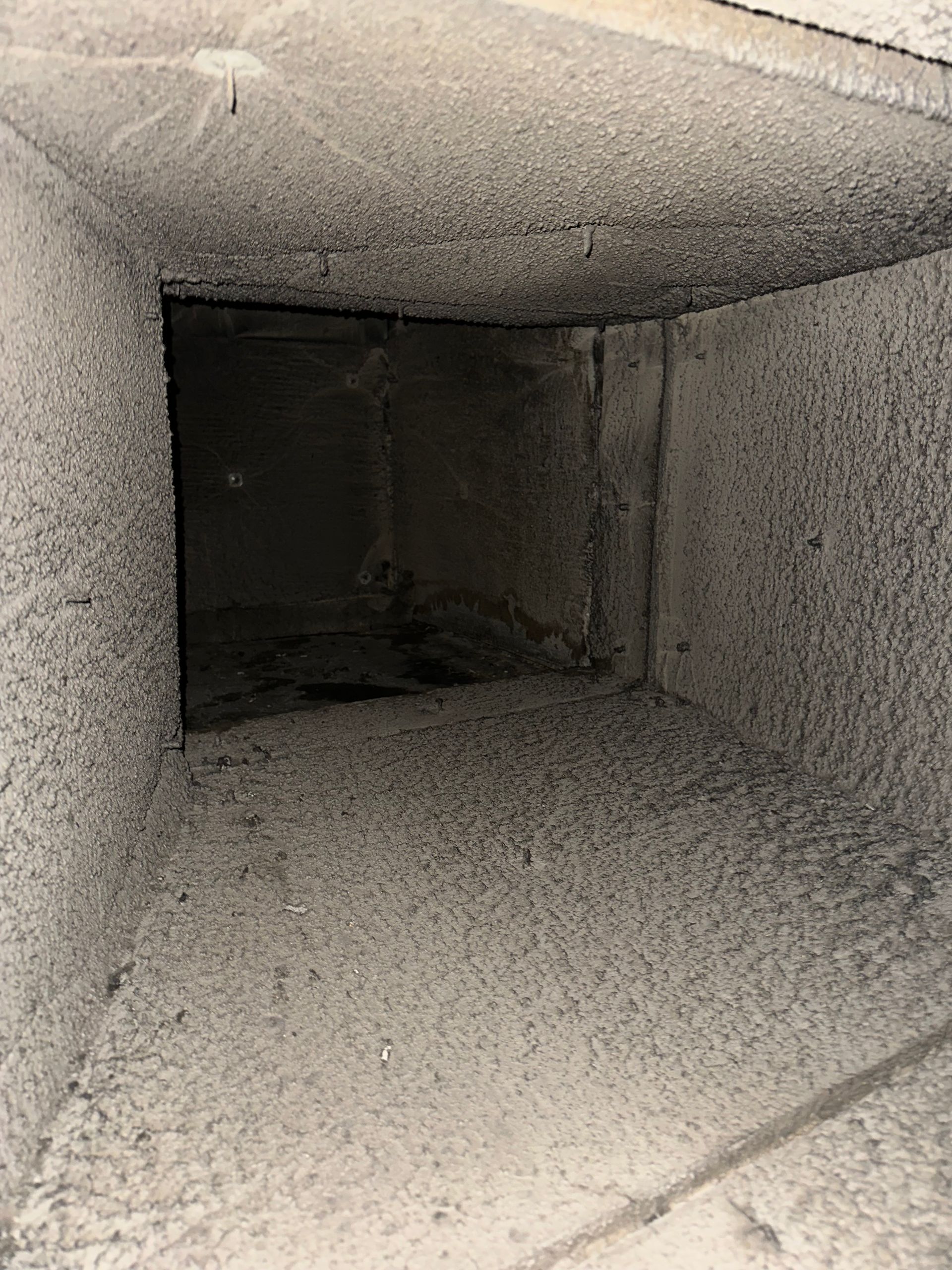 A rectangular air duct interior coated in thick, light-colored dust and debris.