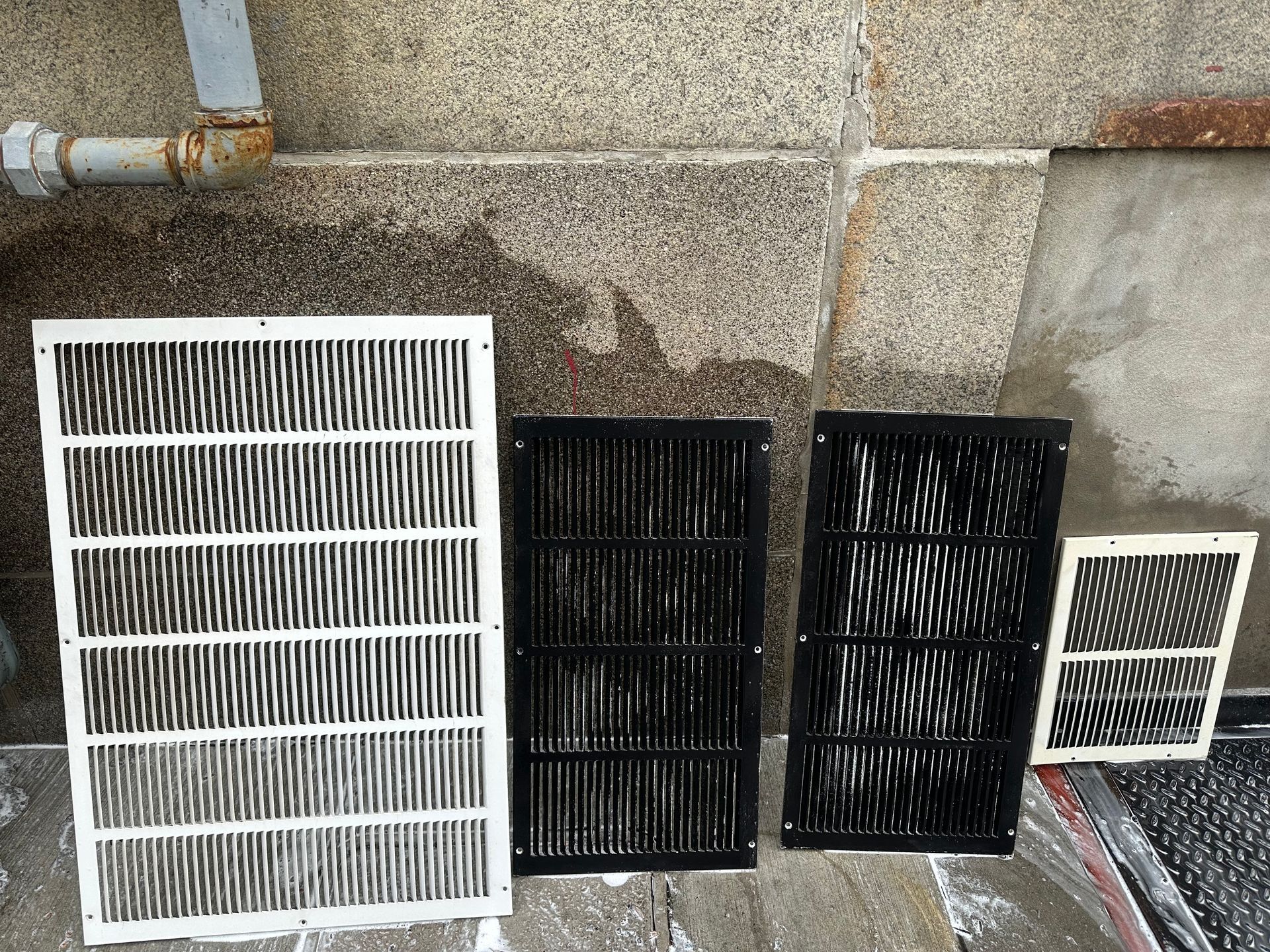 Four air intake grilles of varying sizes and colors against a stone wall.