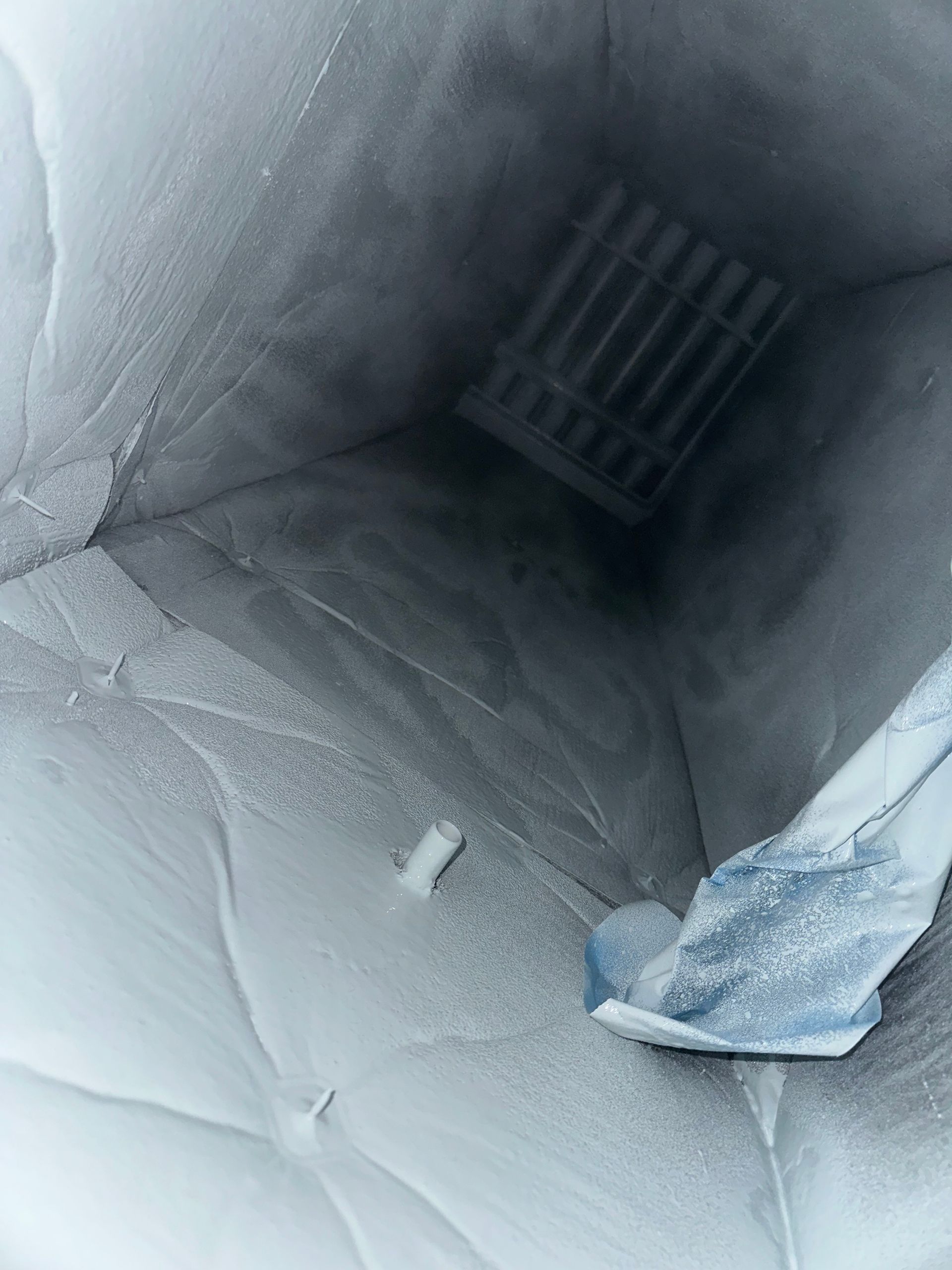 Inside a freezer, looking down into a square interior with a rack at the bottom, heavily frosted.